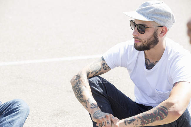 Молодий чоловік з татуюваннями сидить на землі . — стокове фото