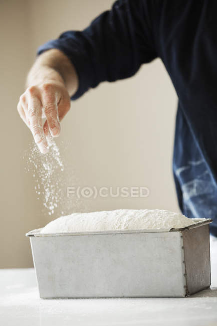 Panadero espolvorear harina sobre la masa de pan - foto de stock