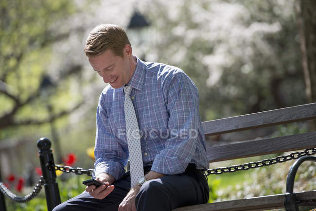 Бизнесмен, сидящий на скамейке в парке — стоковое фото