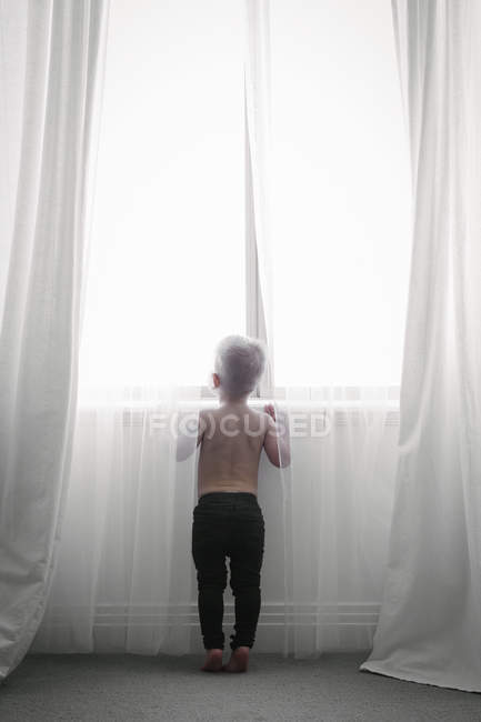 Ребенок смотрит через чистые занавески — стоковое фото