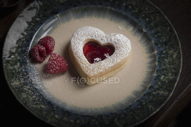 Assiette avec biscuit en forme de coeur et framboises — Photo de stock