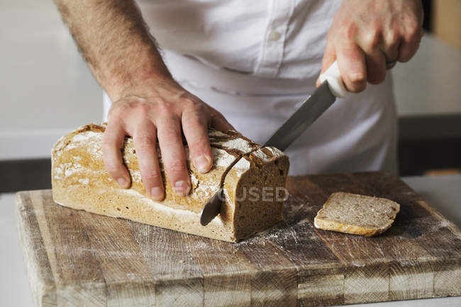 Пекарь нарезает свежеиспеченный хлеб — стоковое фото