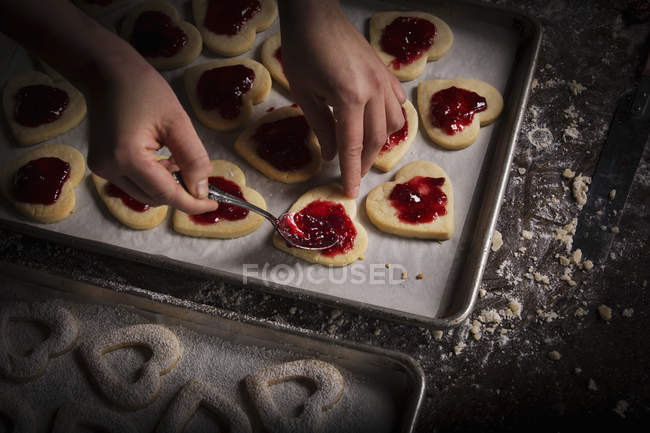 Donna che diffonde marmellata di lamponi sui biscotti — Foto stock