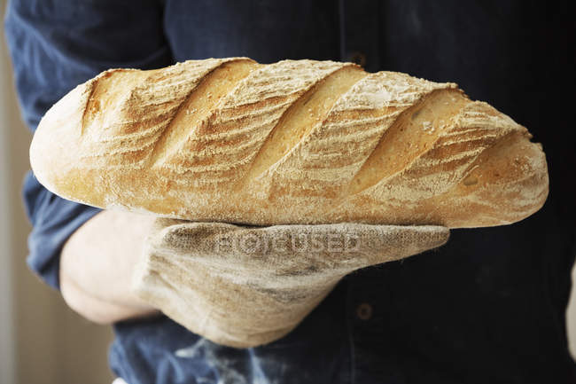 Panadero sosteniendo una barra de pan. - foto de stock