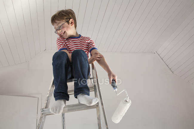 Хлопчик сидить на драбині з малярським валиком — стокове фото