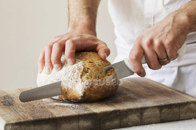 Baker slicing a loaf of bread — Stock Photo