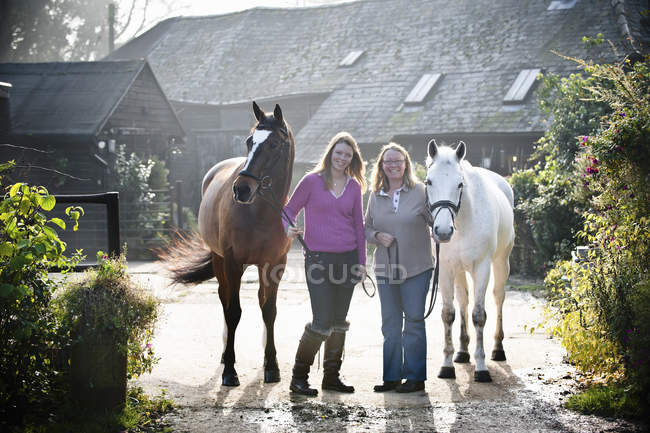 Dos mujeres de pie con caballos - foto de stock