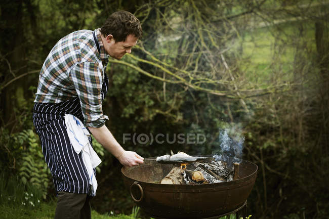 Chef griller un poisson sur un barbecue . — Photo de stock
