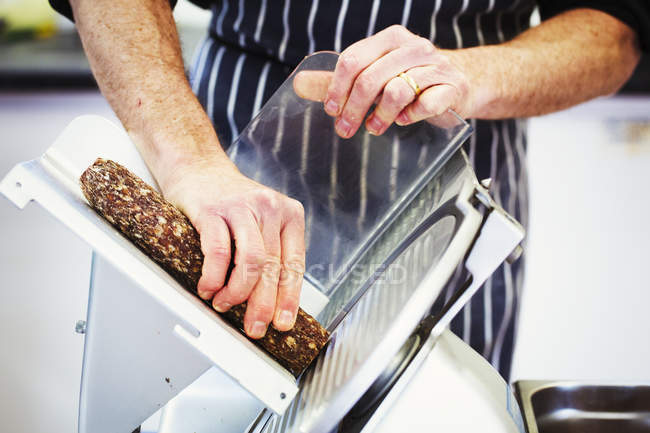 Açougueiro cortando salame com cortador — Fotografia de Stock