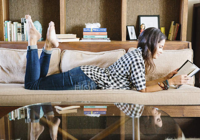 Mujer leyendo un libro en un sofá - foto de stock