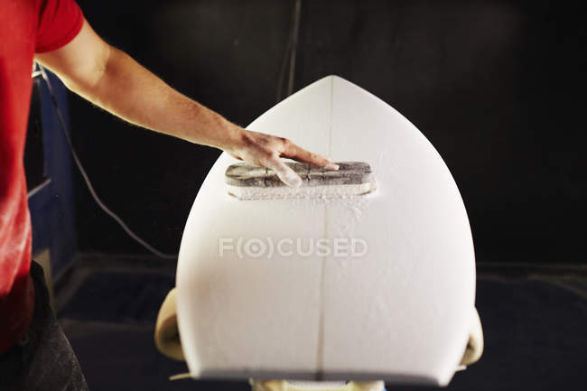 Homme ponçant une planche de surf dans un atelier . — Photo de stock