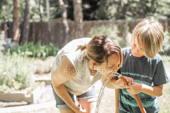 Mother and son drinking water from hose — Stock Photo