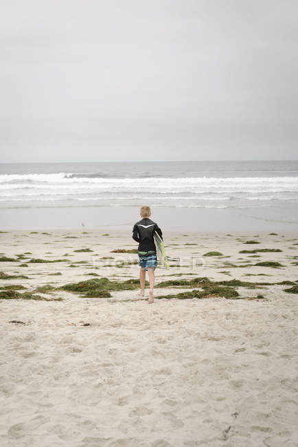 Хлопчик носить кузов і йде в океан — стокове фото