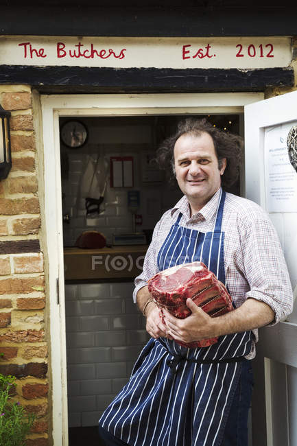 Açougueiro em avental segurando pedaço de carne — Fotografia de Stock
