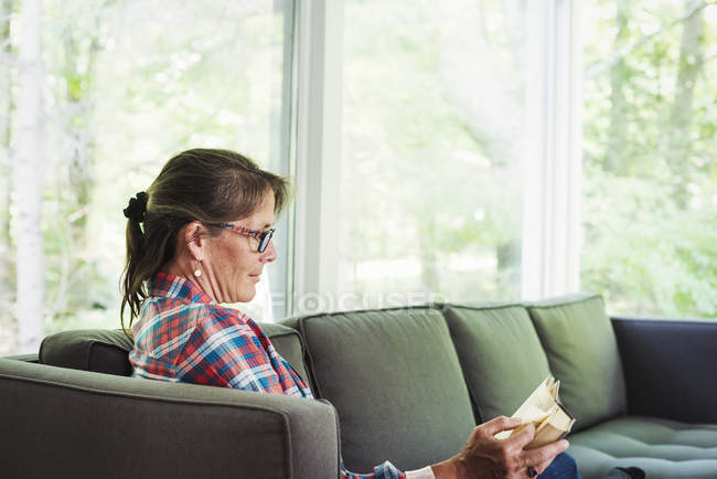 Mujer sentada en un sofá leyendo un libro . - foto de stock