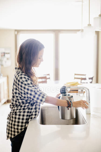 Donna in piedi presso un lavello da cucina . — Foto stock