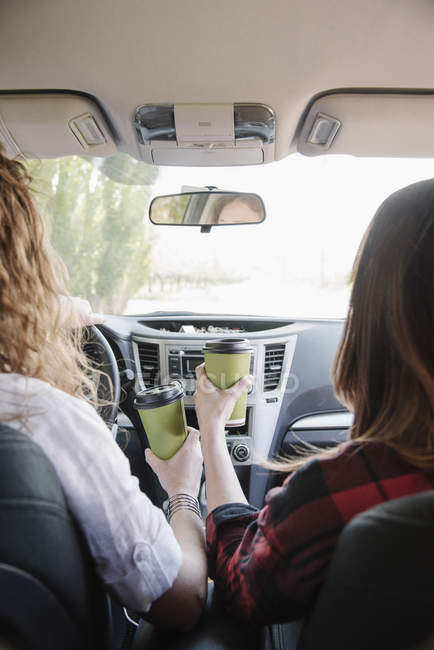 Mujeres en un coche sosteniendo tazas de café - foto de stock