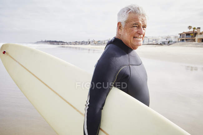 Senior man carrying a surfboard. — Stock Photo