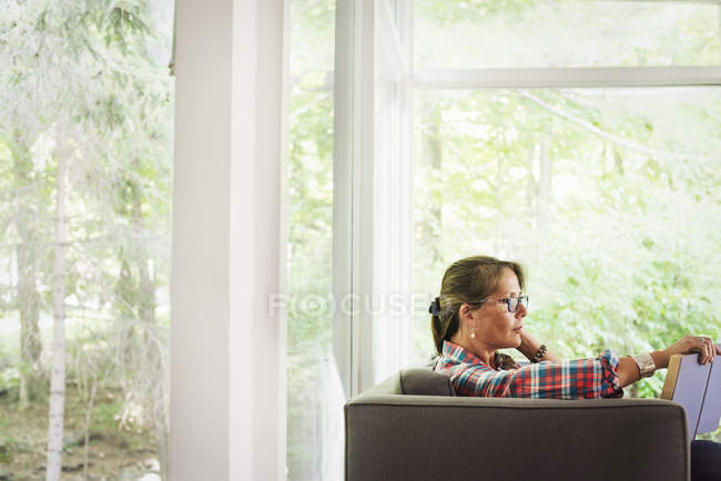 Femme assise sur un canapé lisant un livre . — Photo de stock