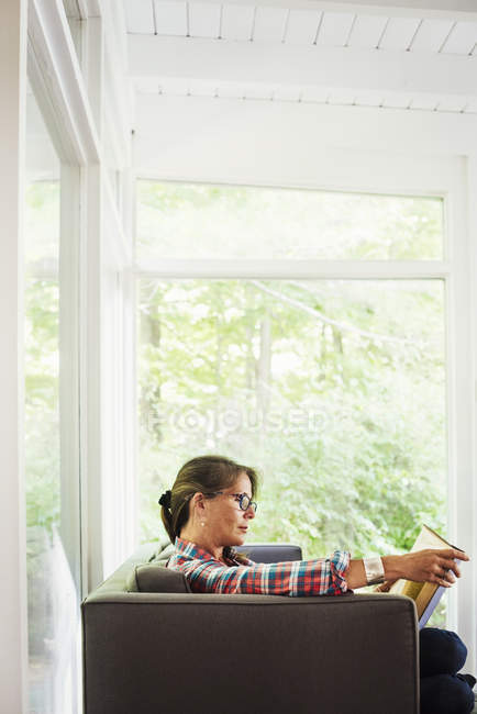 Frau sitzt auf einem Sofa und liest ein Buch. — Stockfoto