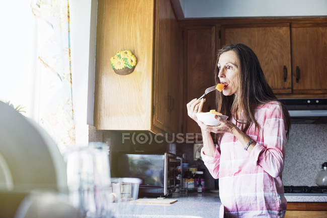 Senior woman eating in a kitchen — Stock Photo