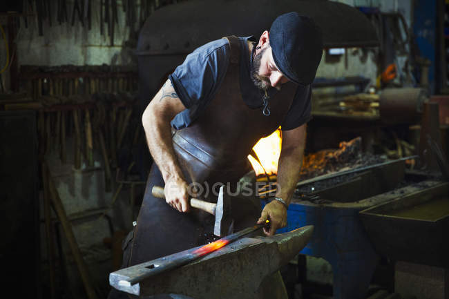 Blacksmith holds a length of hot metal — Stock Photo