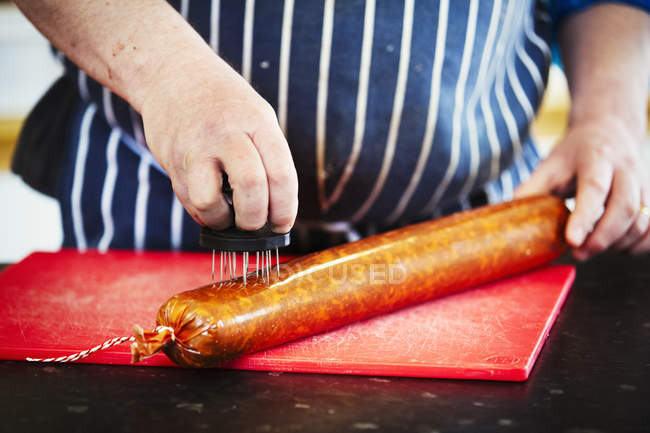 Butcher pricking holes into of Chorizo sausage — Stock Photo