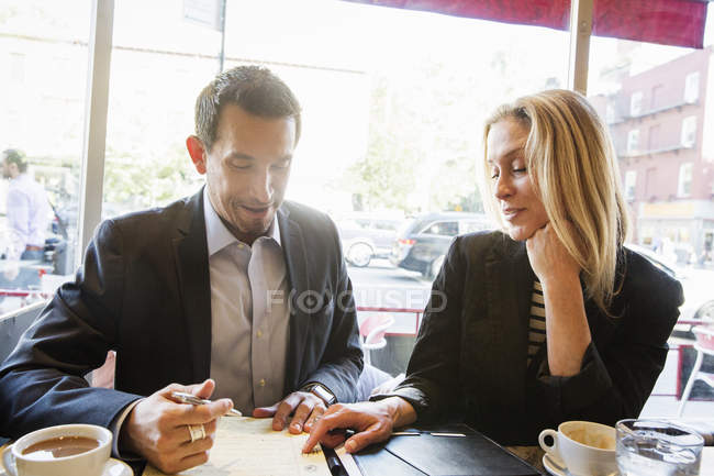 Empresaria y hombre de negocios sentado a la mesa en la cafetería - foto de stock