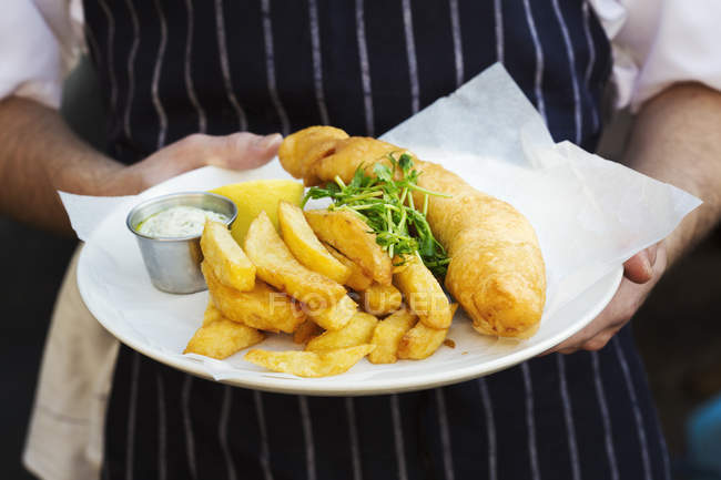 Waiter holding dish of fish and chips — Stock Photo