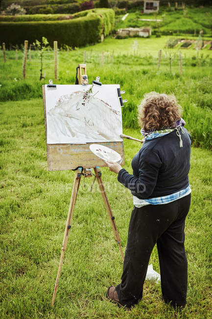 Femme artiste debout à l'extérieur à un chevalet — Photo de stock