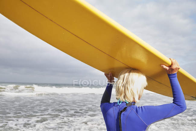 Senior woman carrying a surfboard — Stock Photo