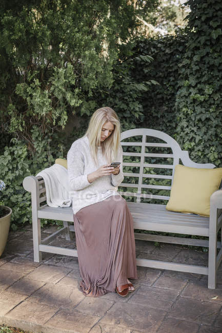 Mujer sentada en un jardín en un banco - foto de stock