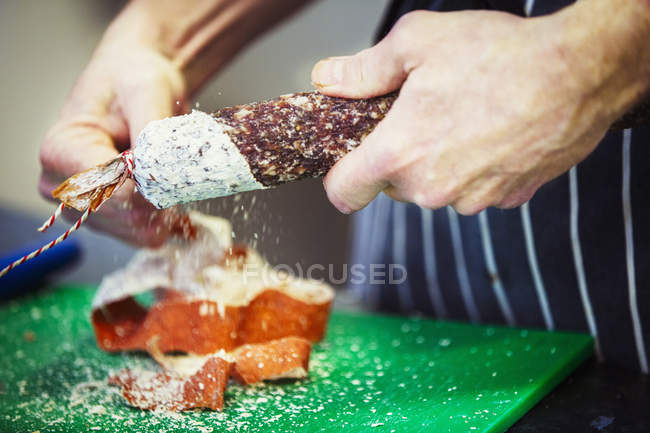 Carnicero quitando la piel de salami - foto de stock