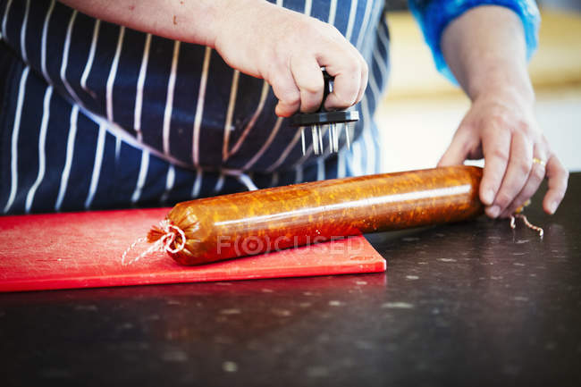 Carnicero pinchando agujeros en de chorizo salchicha - foto de stock