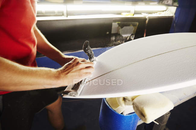 Hombre trabajando en una tabla de surf en un taller . - foto de stock