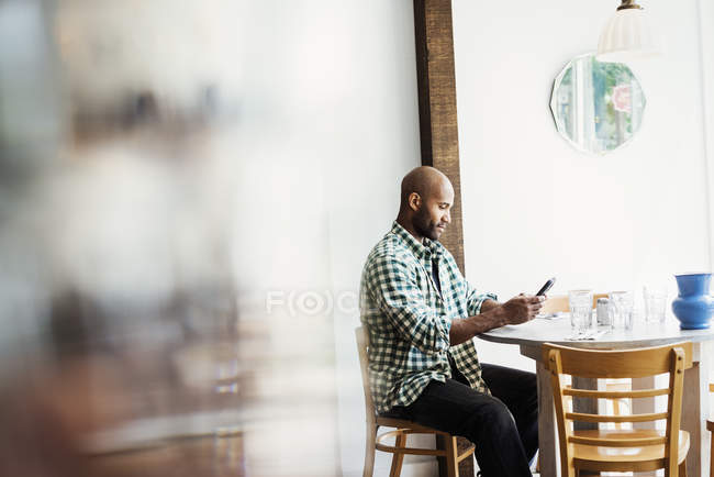 Мужчина сидит в кафе и пользуется телефоном — стоковое фото
