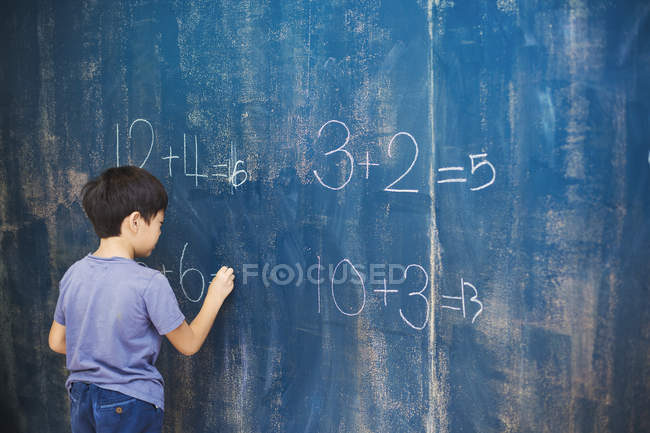 Niño escribiendo con tiza en una pizarra . - foto de stock