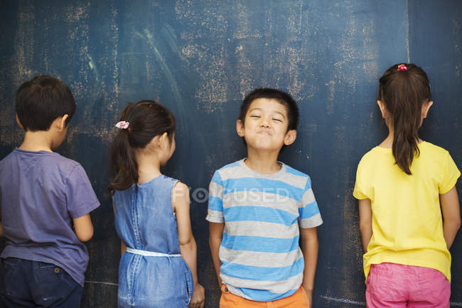 Four children standing by the blackboard. — Stock Photo