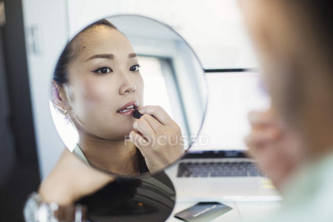 Woman putting on lipstick and holding a mirror. — Stock Photo