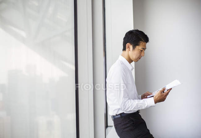 Geschäftsmann vor einem großen Fenster beim Lesen von Papieren. — Stockfoto