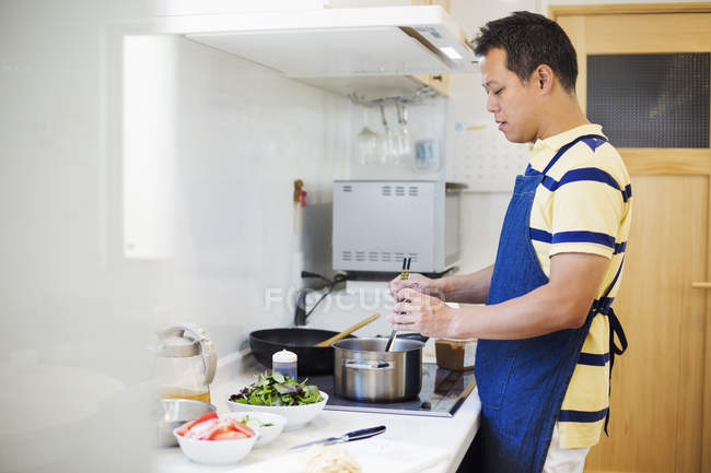 Mann in blauer Schürze bereitet eine Mahlzeit zu. — Stockfoto