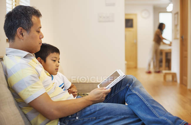 Hombre e hijo sentado leyendo un libro . - foto de stock