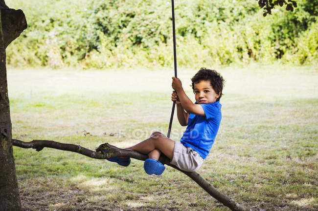 Menino sentado em um balanço de árvore . — Fotografia de Stock