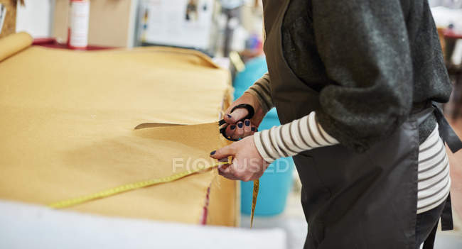 Woman cutting out yellow upholstery fabric — Stock Photo