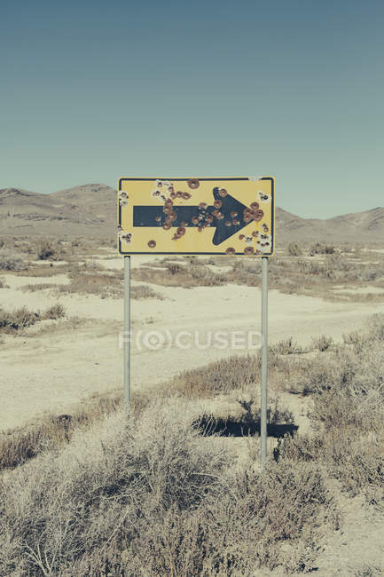 Señal de flecha acribillada en el desierto - foto de stock