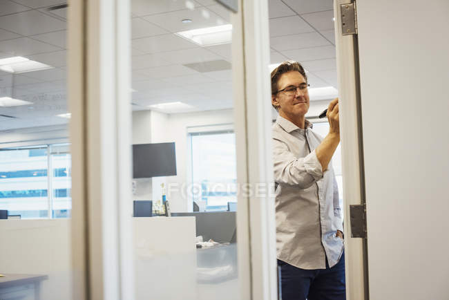 Homem de pé no escritório escrevendo no quadro branco — Fotografia de Stock