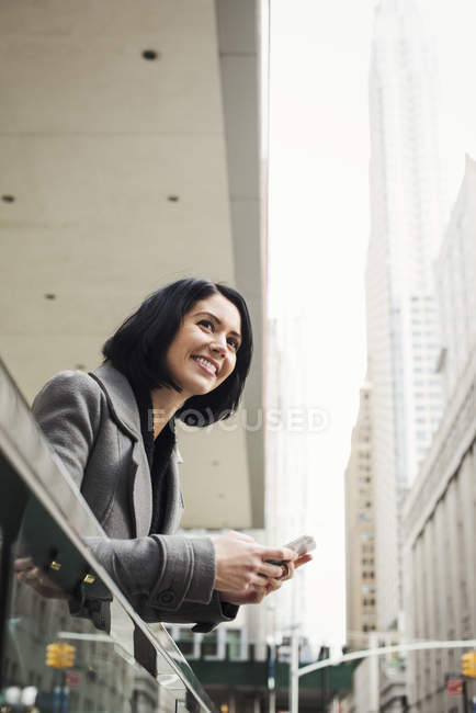 Frau lehnt sich über Balkon und hält Handy in der Hand — Stockfoto