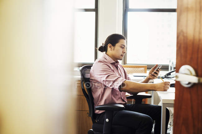 Homem sentado no escritório e verificando o telefone , — Fotografia de Stock