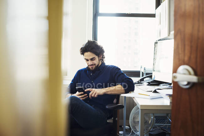 Человек сидит в офисе и проверяет телефон , — стоковое фото