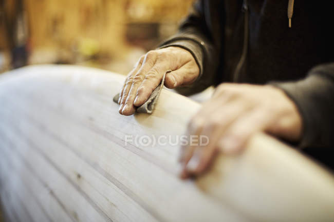 Man sanding edge of wooden surfboard. — Stock Photo